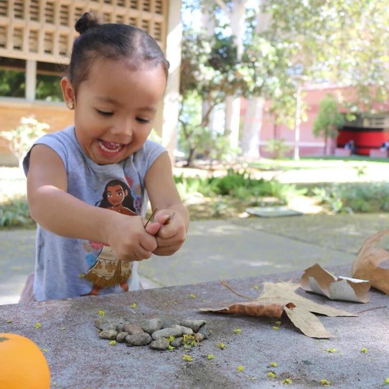 Small child at 十大网赌网址平台首页 campus playing with leaves and rocks